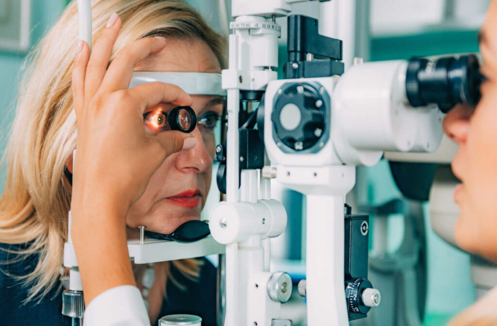 An eye doctor holding a small magnifying lens performs a slit lamp test on a female patient.