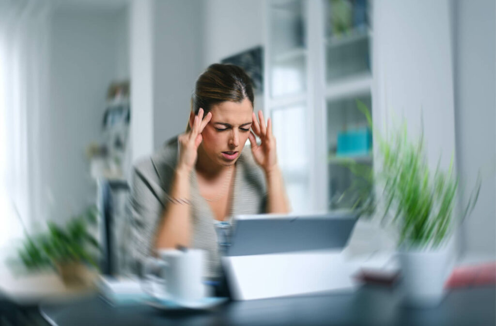 A working woman with throbbing headache and visual aura, signs of migraine with aura, is holding the sides of her head.