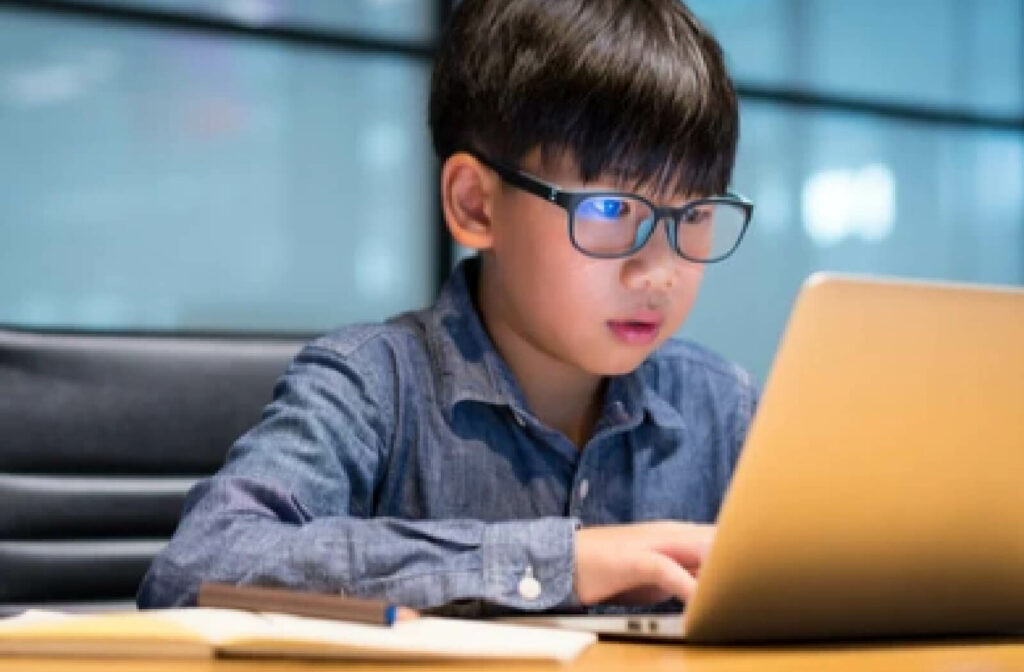 A boy wearing protective eyeglasses to prevent blue lights from his gadget.