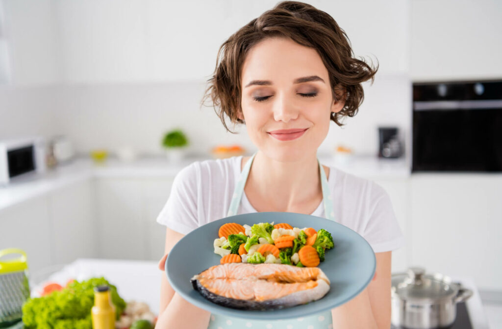 A woman is showing delicious plated salmon and vegetables. Good food for the eyes