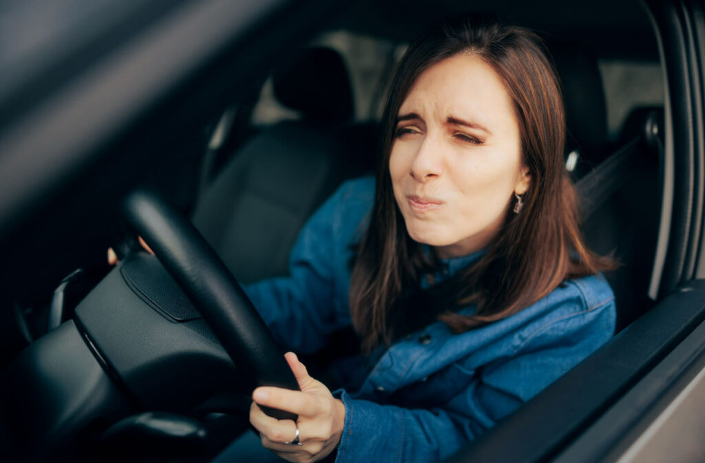 A woman is squinting to see clearly her way while driving a car. Squinting is a symptoms of astigmatism.