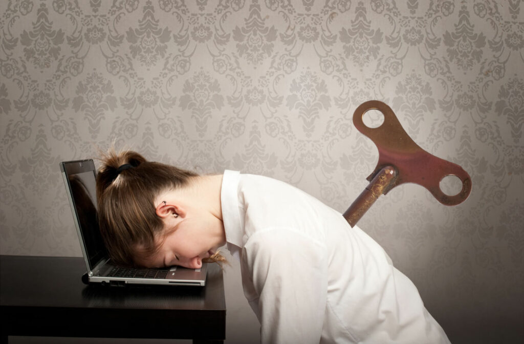 A young girl with a key winder on her back sleeping on her laptop is lack of energy to continue her work.