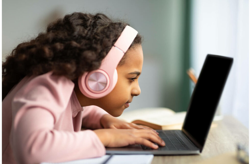 A side view of a child with headphones using a laptop very close to her face