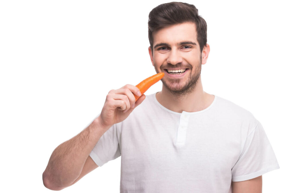A man holding a carrot on his right hand, looking directly at the camera and smiling.