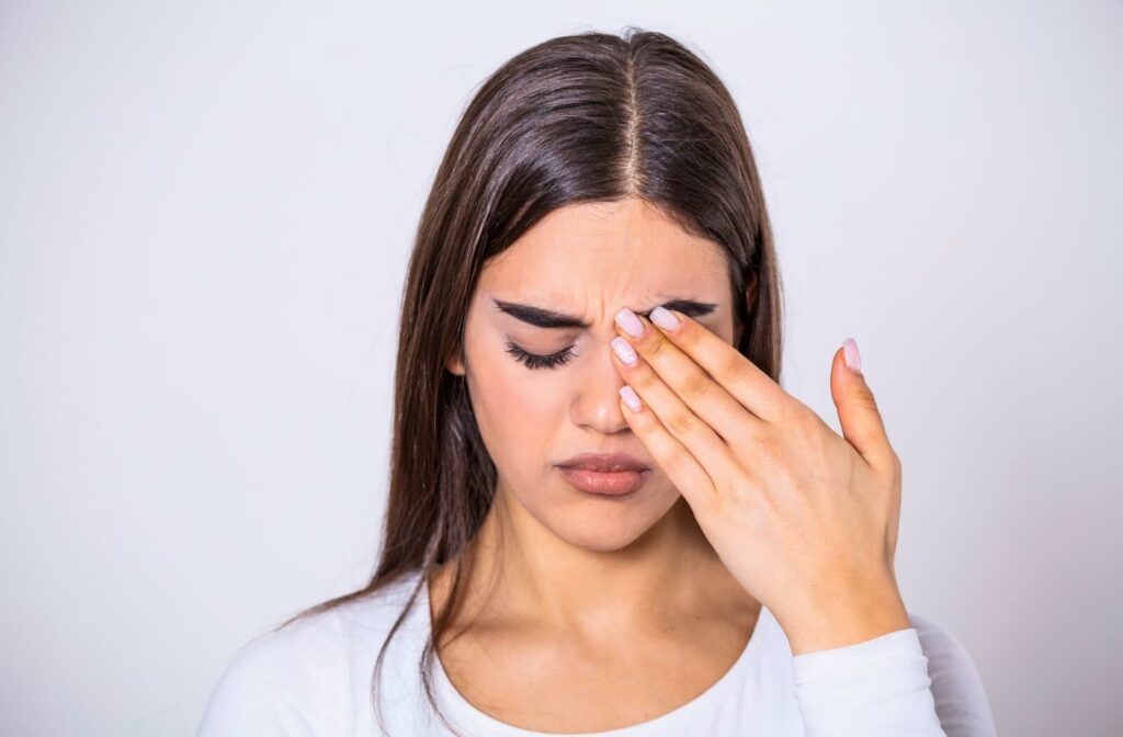 A woman with make up rubbing her left eye with her left hand.