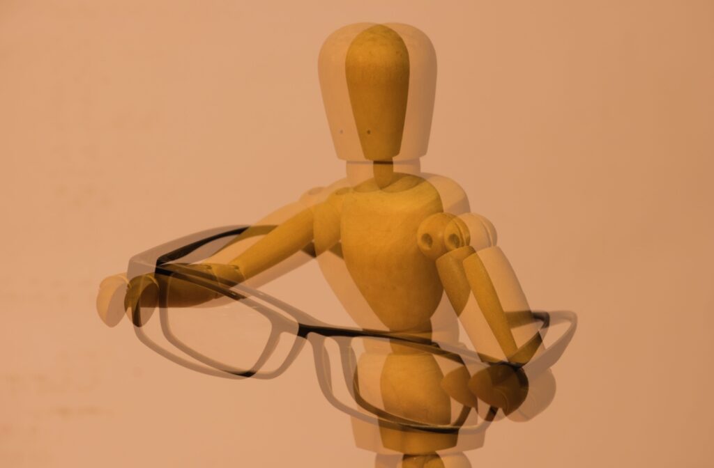 A close-up of a wooden doll holding glasses illustrates what double vision looks like.