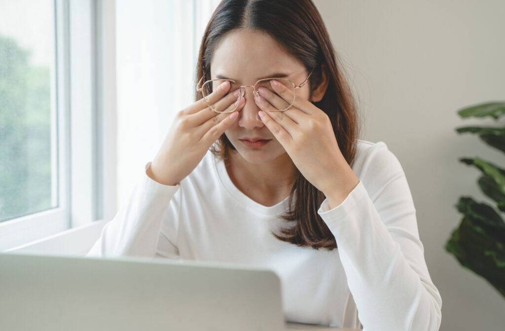 An image of a person working on their computer and rubbing their eyes because they are in pain.