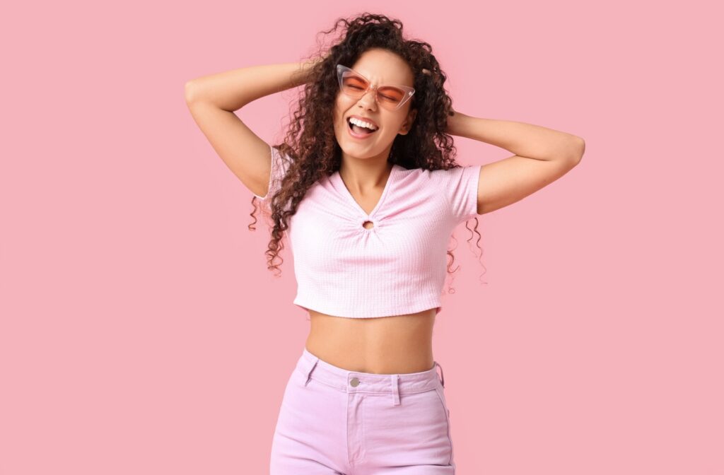 A happy person standing against a pink background wearing pink tinted glasses.