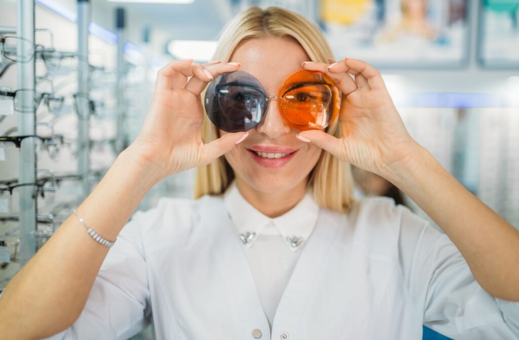 A smiling optician holding an orange and grey tinted lens in front of their eyes.