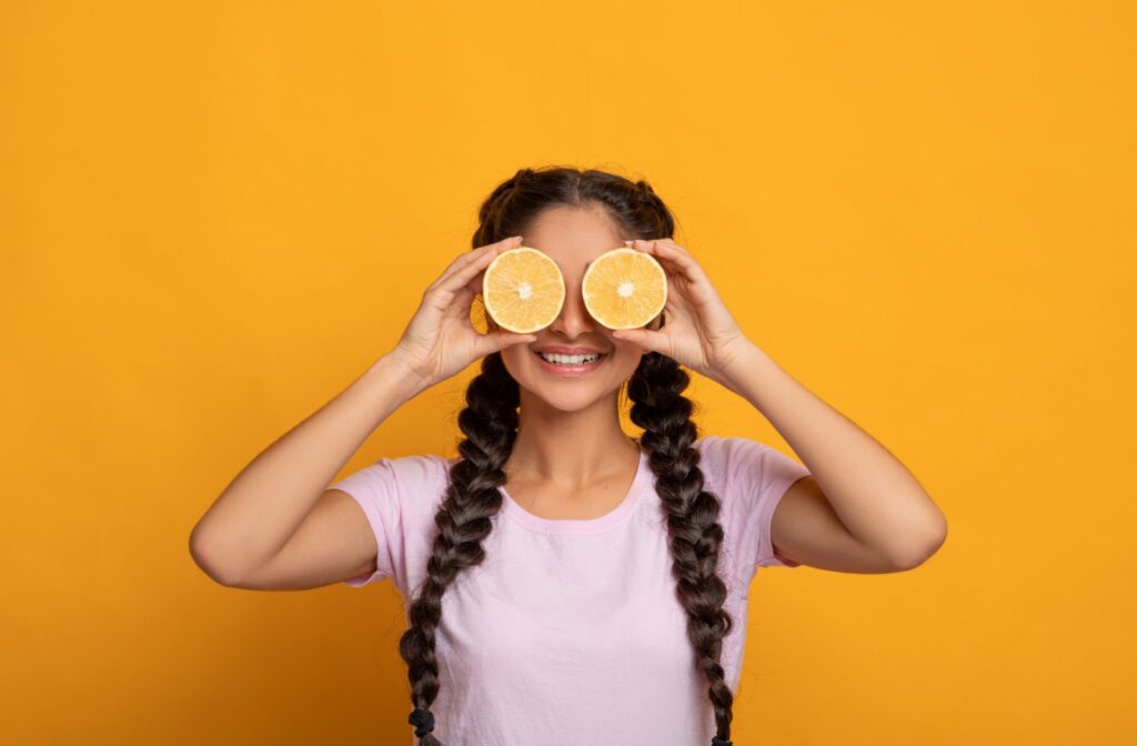 A smiling person holds up two halves of a citrus fruit in front of their eyes.