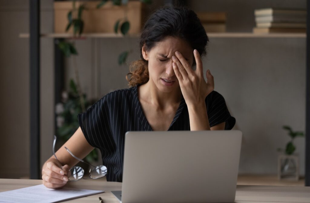 Someone working on a computer rubs their forehead due to a headache from eye misalignment.