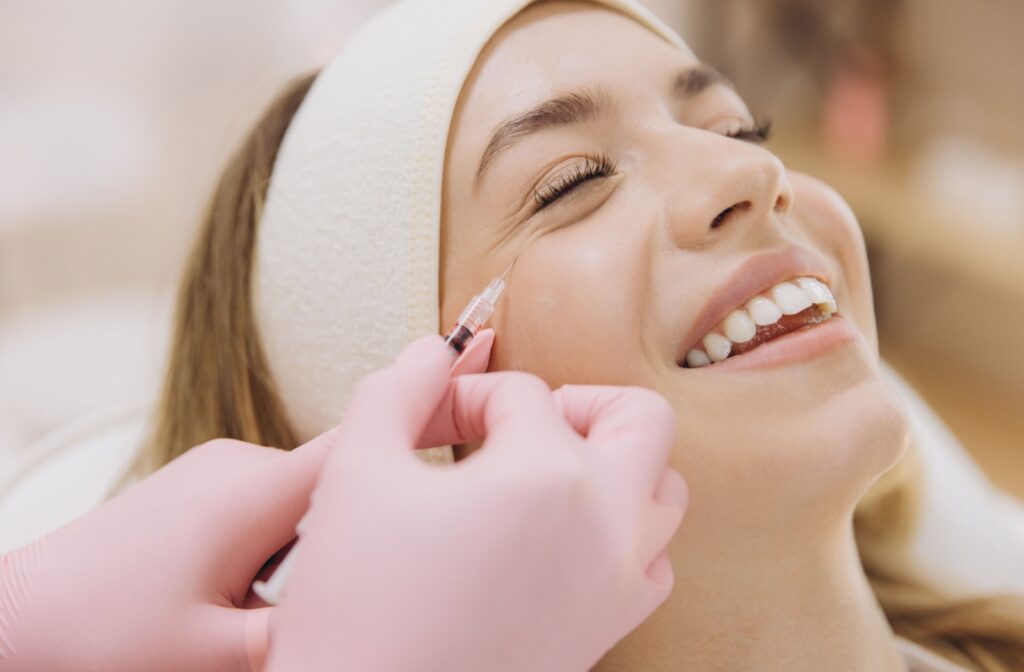 Professional aesthetician performing botox injection, treating wrinkles on smiling female client's skin during cosmetic procedure.