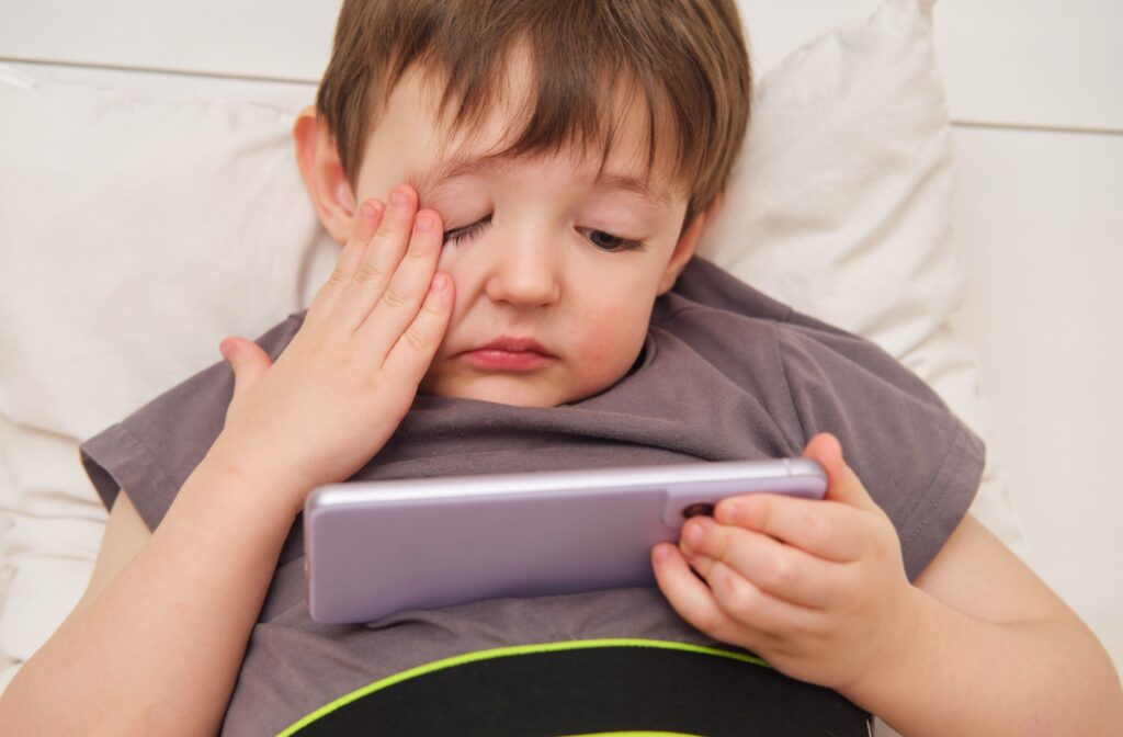 A young kid rubbing their eye while staring at a screen.