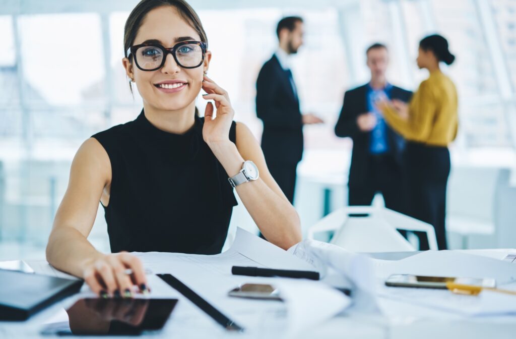A person sitting at their desk at work, wearing a pair of glasses picked and fitted for long days and work and commuting.