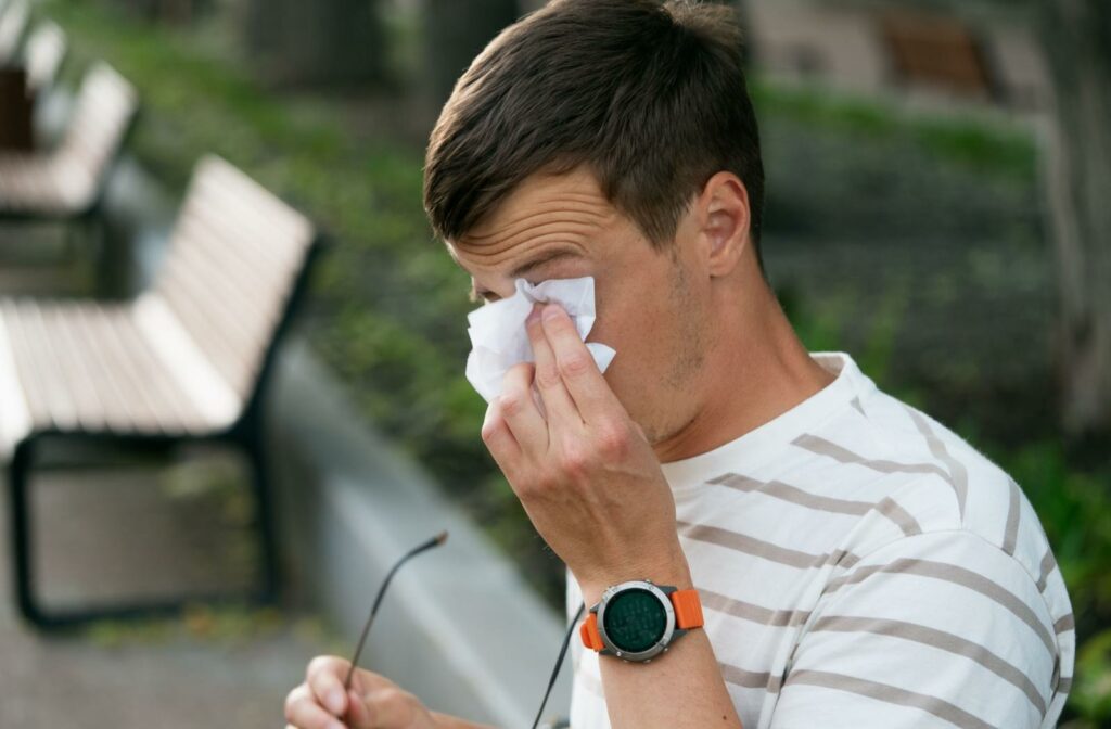 A person wiping their watery eye with a tissue.